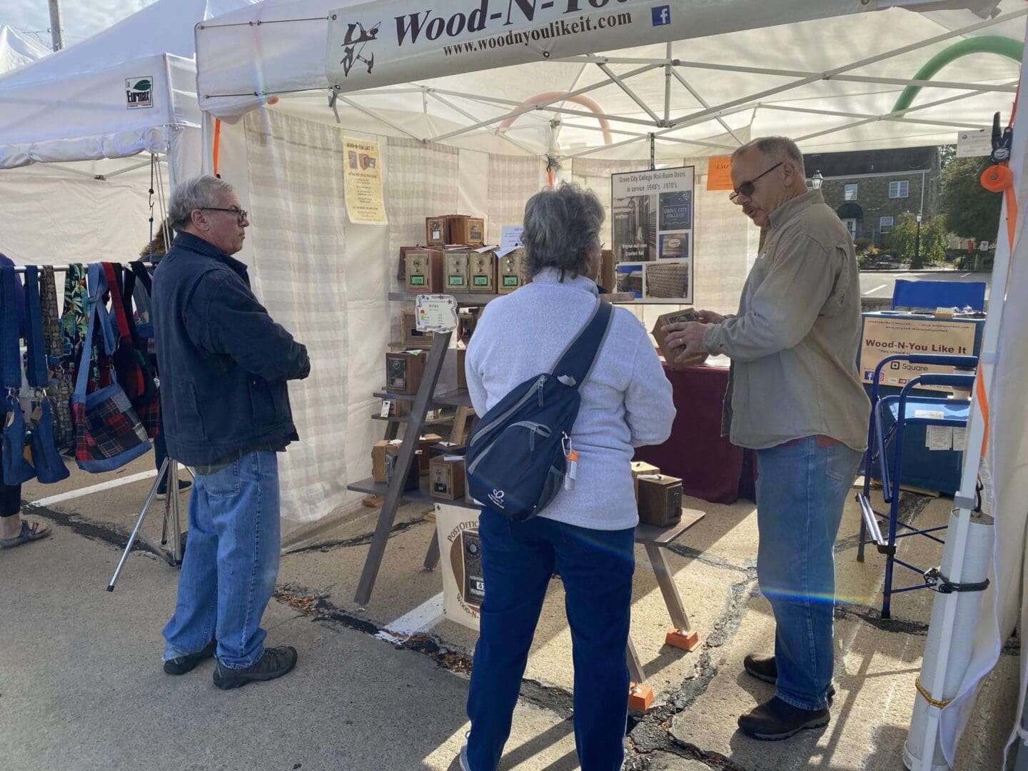 Three people standing around a tent with wood art on it.