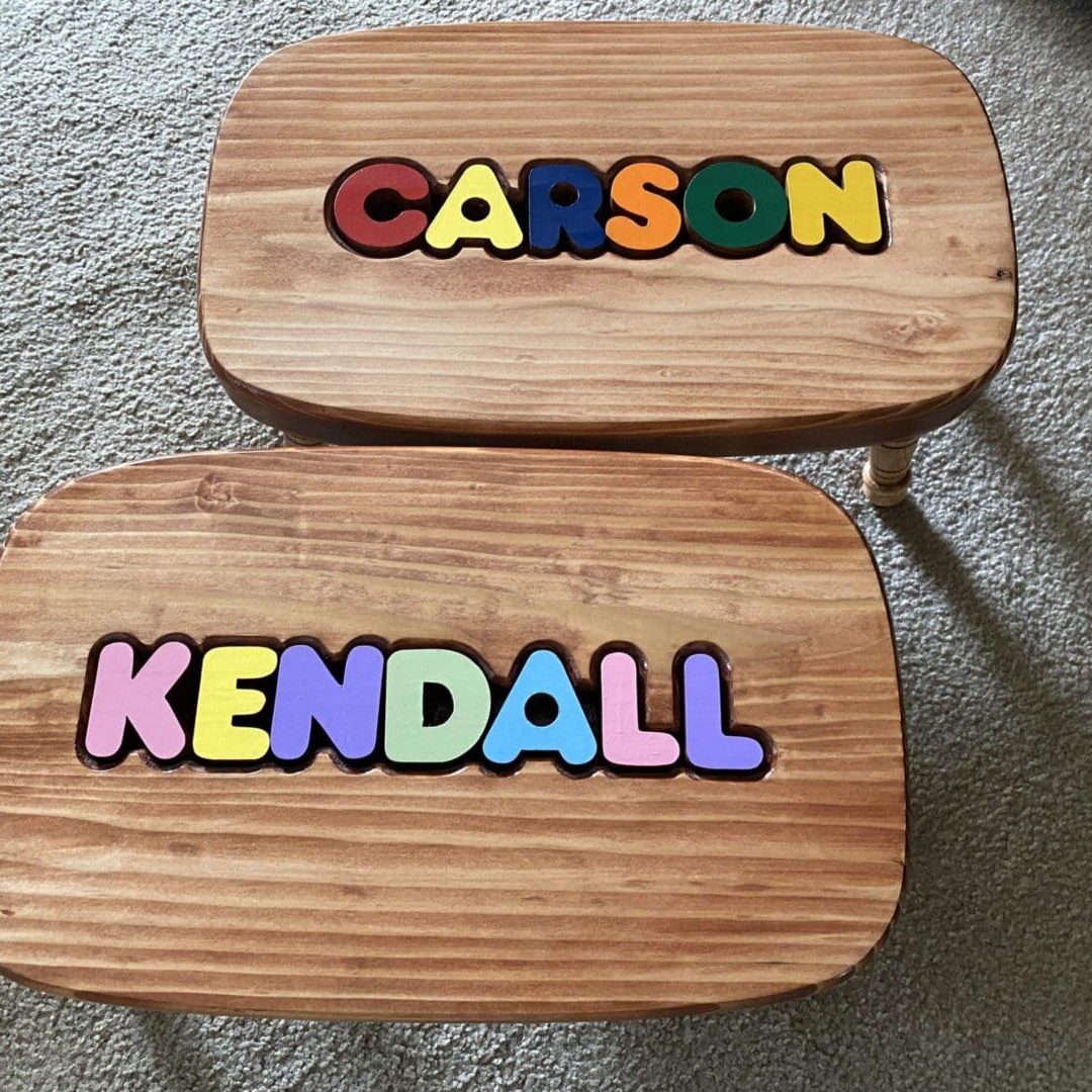 A pair of wooden name puzzles sitting on the floor.